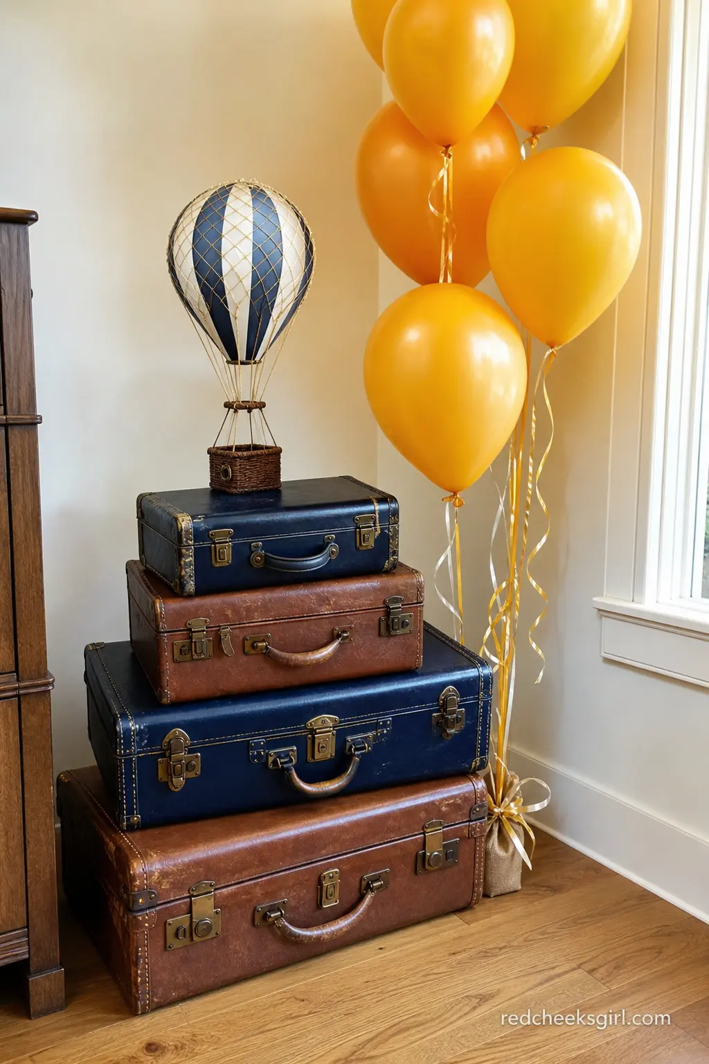 Vintage Suitcase Stack Photo Corner — Stacked vintage-style suitcases in navy and brown, topped with a small striped hot air balloon model and a cluster of