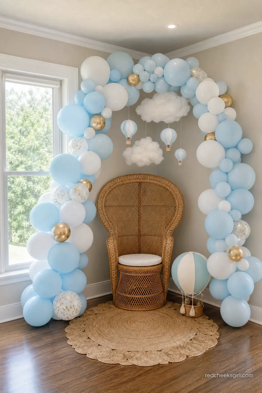 Wicker Chair Sky Nook — A wicker peacock chair tucked under a sky blue and white balloon garland, with a few cotton cloud shapes floating above, gives guests a