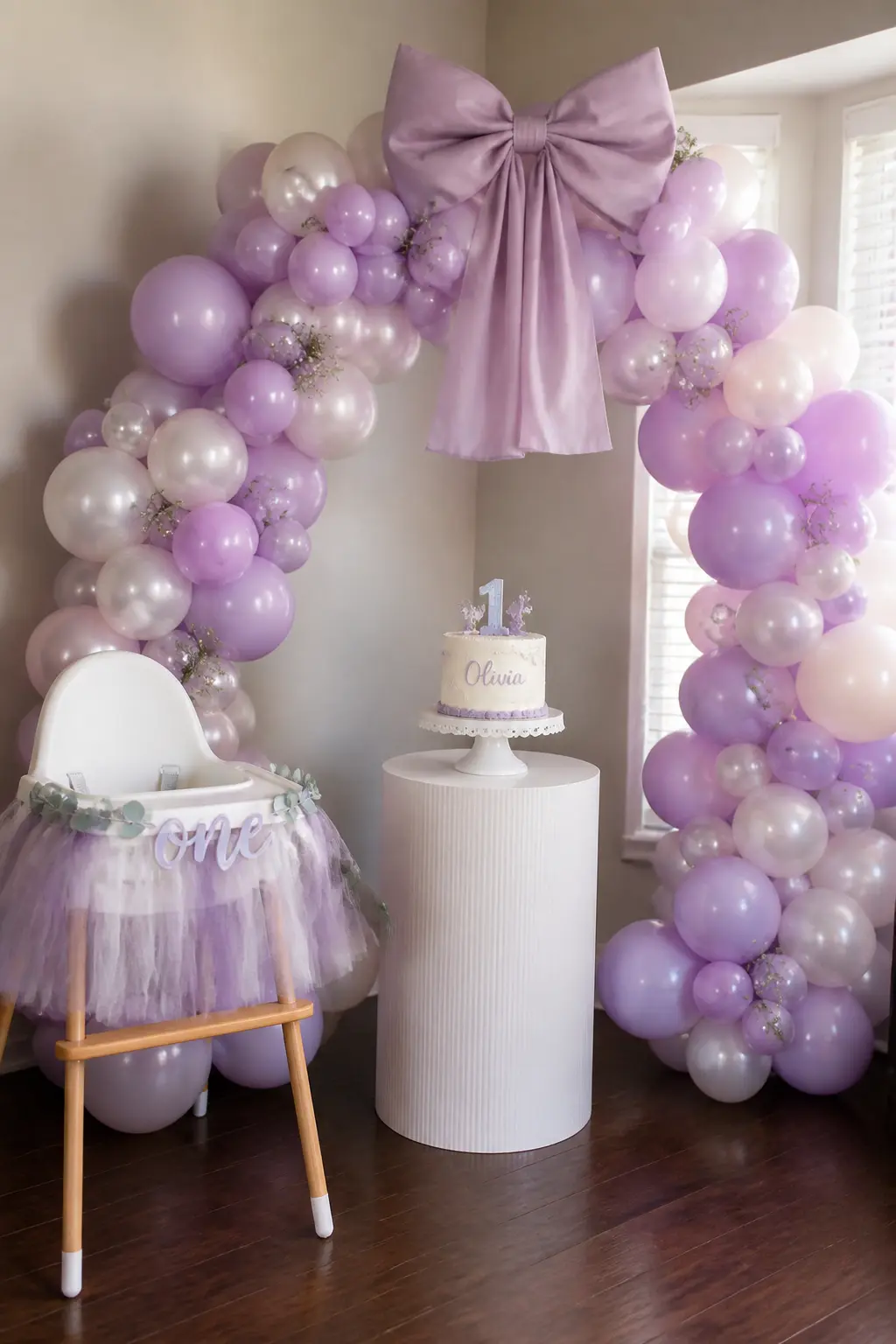 Lavender and Pearl Arch Behind a First Birthday Cake with a Fabric Bow — A first birthday straddles the line between adult aesthetics and child-adjacent