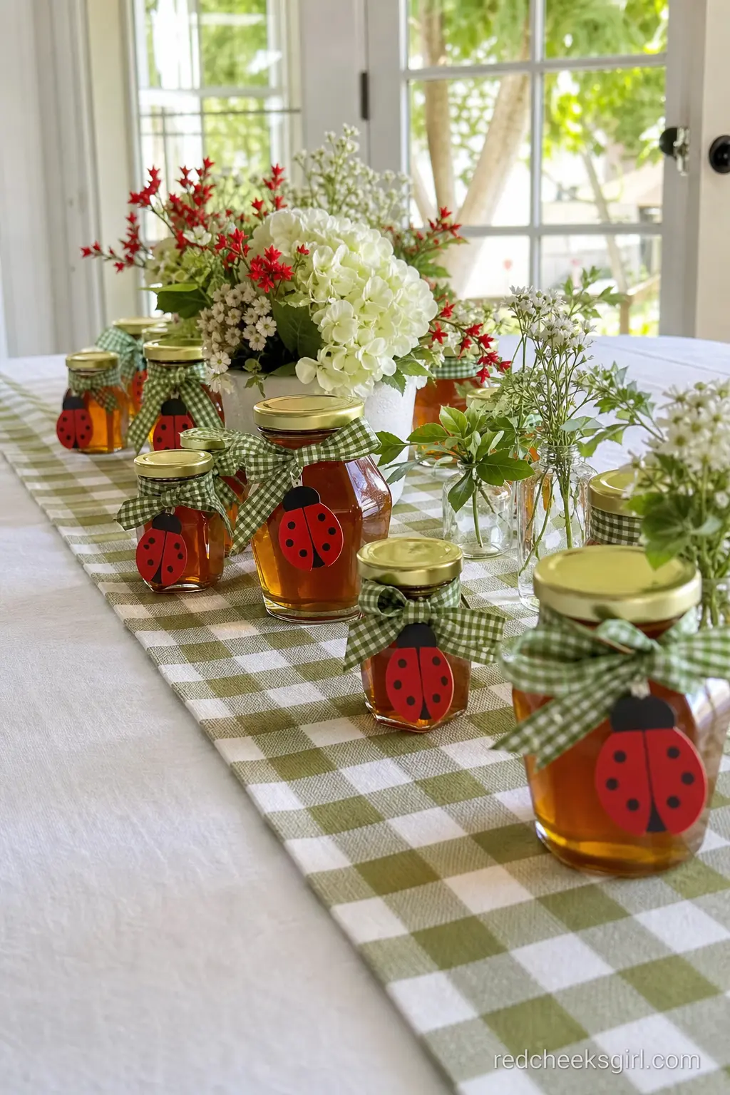 Honey Jar Centerpiece Row — A line of small honey jars in amber gold, each tied with a moss green gingham ribbon and a red ladybug gift tag, runs down the