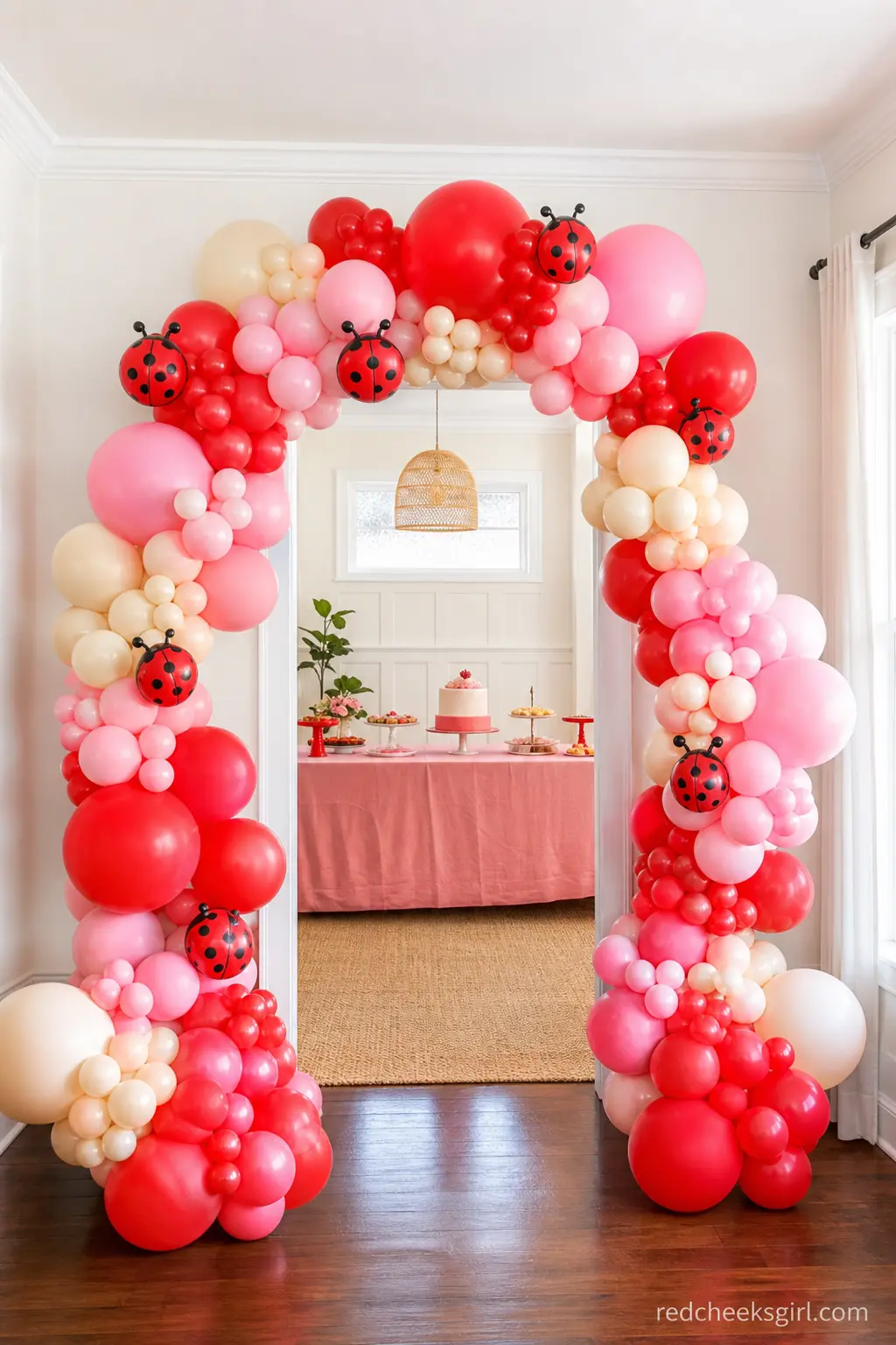 Ladybug Color Balloon Arch — An organic balloon arch in red, pink and ivory curves over the entrance, mixing sizes so it looks gathered rather than gridded.