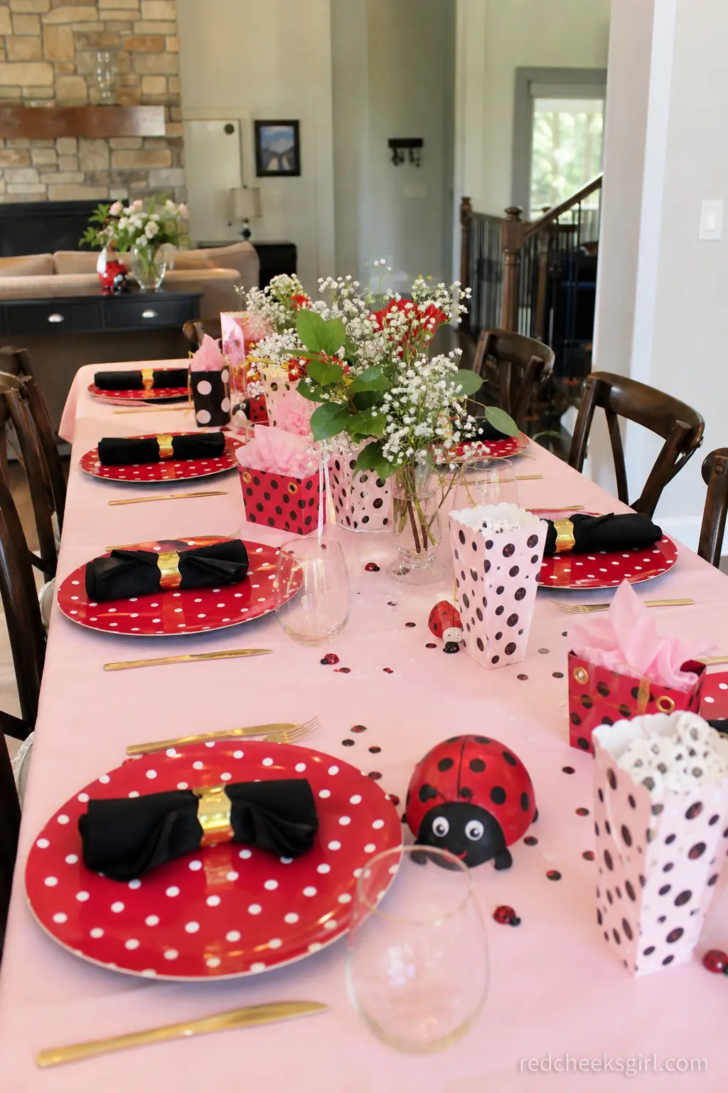 Polka Dot Table Setting — A blush pink tablecloth holds red polka dot chargers, black cloth napkins and gold flatware at each place, laid out along the full