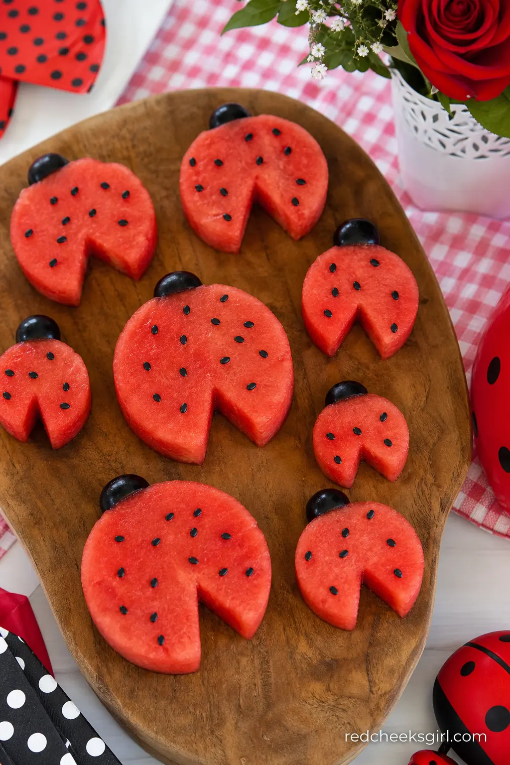Watermelon Ladybug Fruit Platter — Watermelon rounds carved into ladybug shapes, with black sesame seed dots pressed into the red flesh, fill a wooden serving