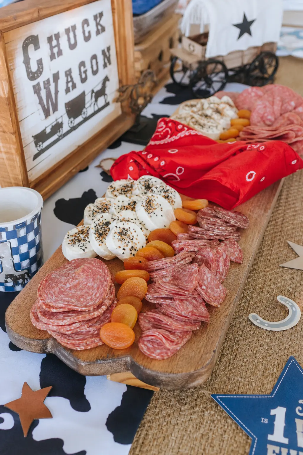 Chuck Wagon Charcuterie Board Spread — A long wooden board spread with cured meats, cream cheeses and dried fruit, arranged in loose rows rather than tight