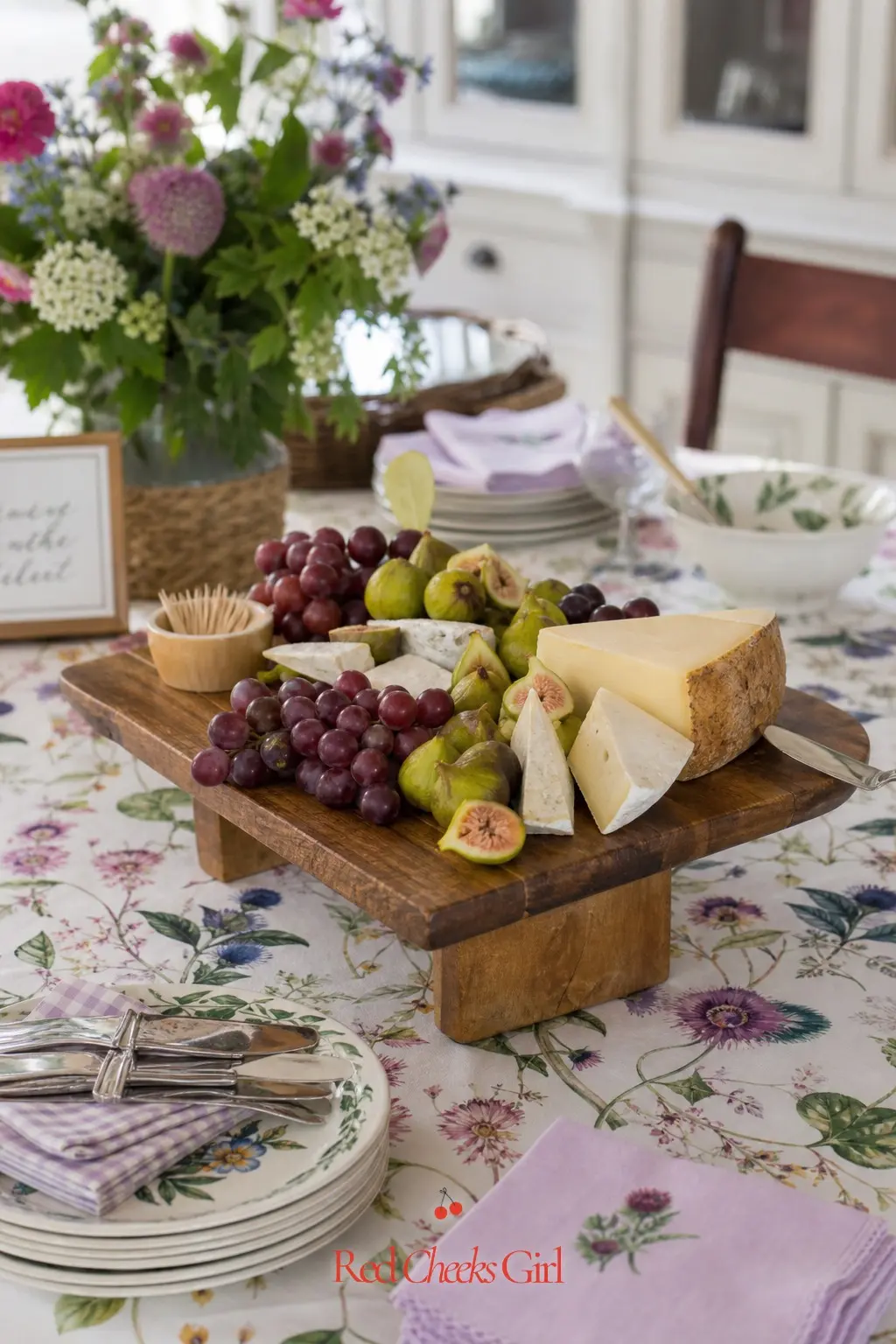 Farmers Market Cheese and Fruit Board — A wooden board loaded with purple grapes, green figs and a few cheese wedges, set on its own small stand, gives guests