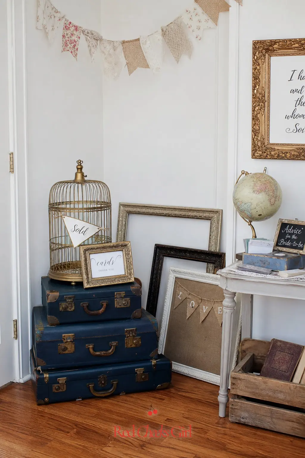 Flea Market Vignette Corner — A stack of navy vintage style suitcases, a brass birdcage tagged sold, and a few mismatched frames leaning against the wall turns