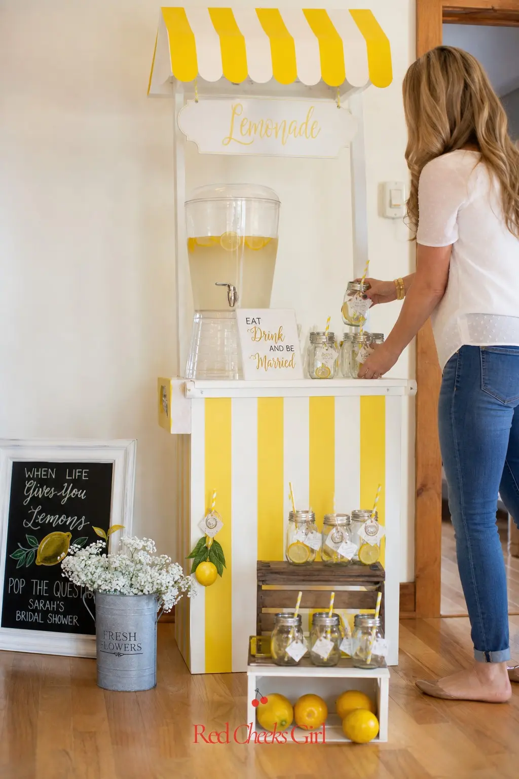 Lemonade Stand Drink Station — A small yellow and white striped stand holding a glass dispenser and a row of mason jar glasses covers drinks without needing a