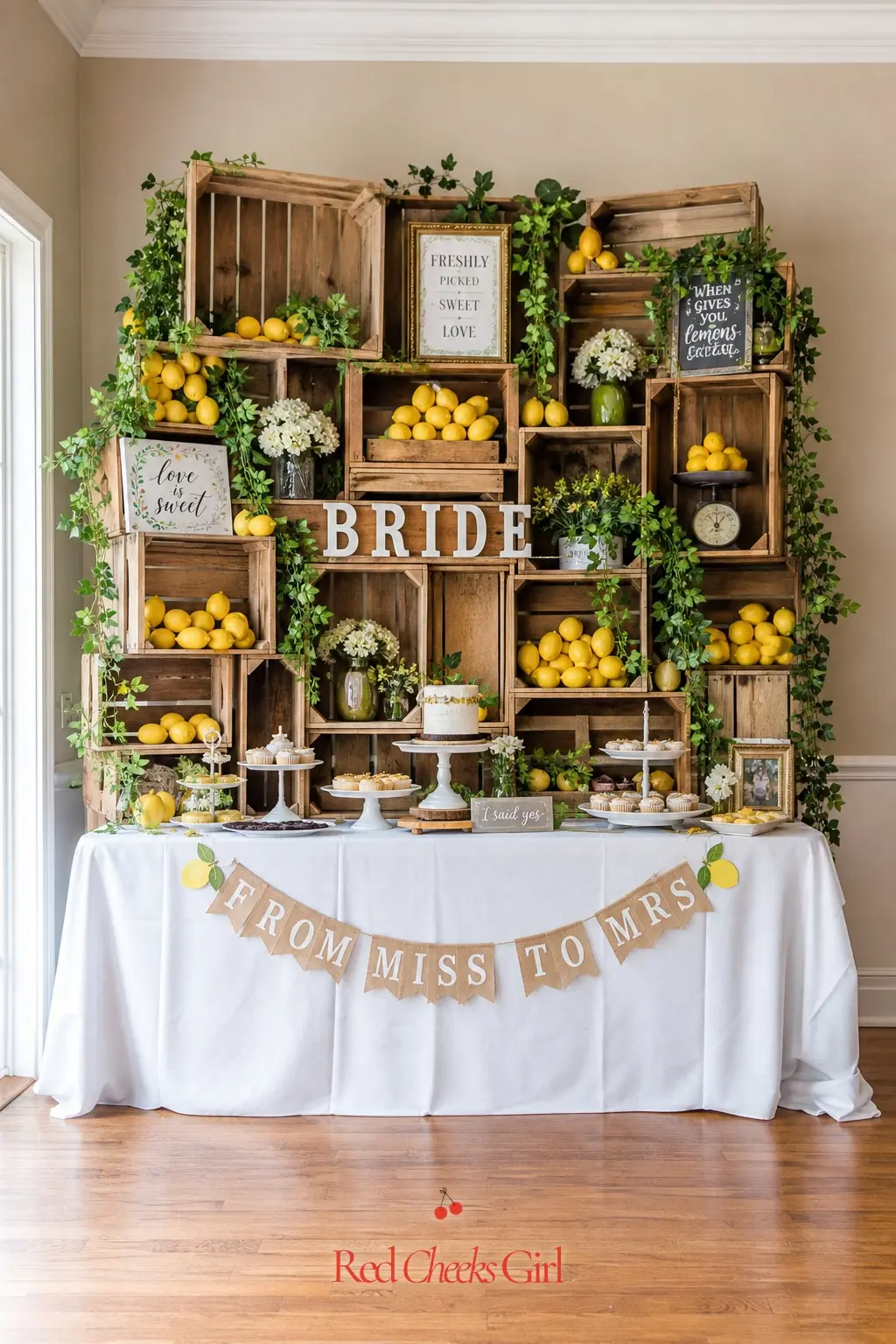 Produce Crate Backdrop Wall — Stacked wooden crates filled with lemons and trailing vine turn a plain wall behind the dessert table into a genuine stall front.