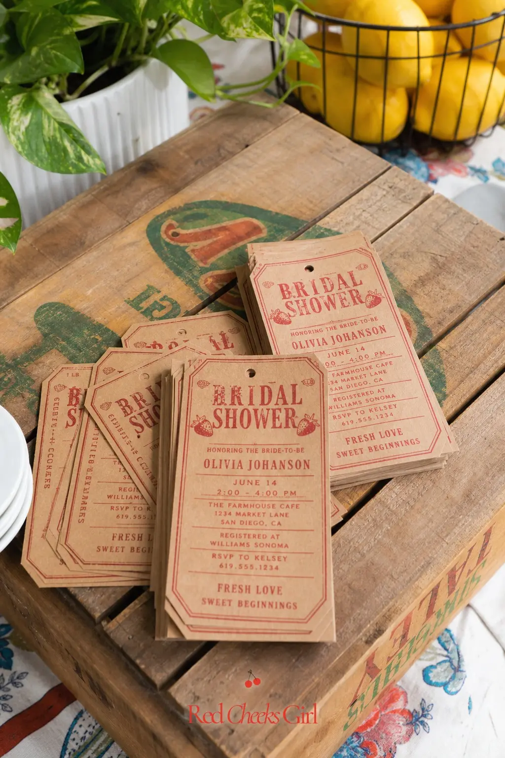 Produce Stamp Invitation Display — Kraft paper invitations stamped in red ink to look like produce tags, laid out on a crate lid for guests to admire on their