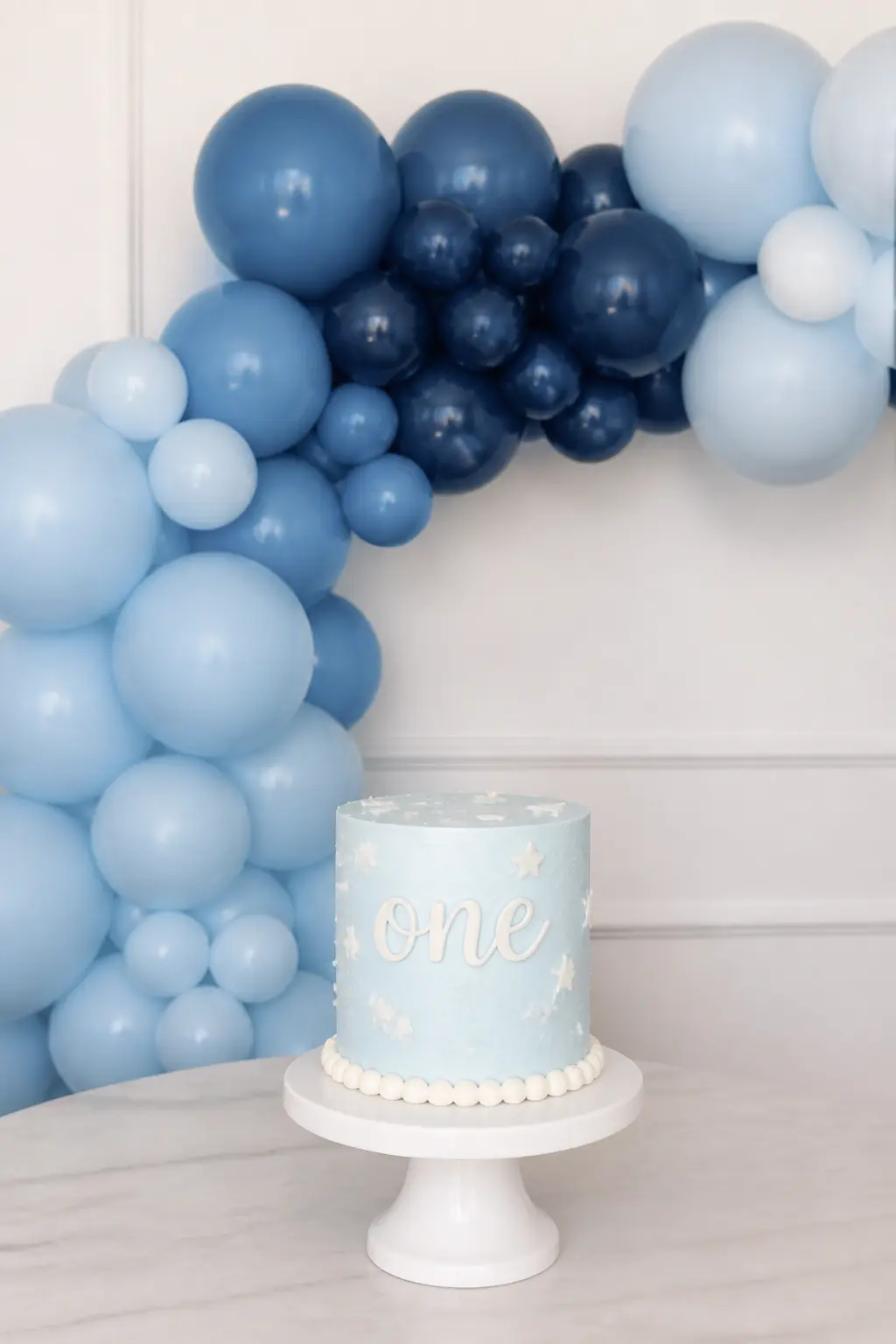 Powder Blue to Navy Behind a First Birthday Cake — A garland rather than a full arch works better behind a small cake table: it stays in frame without