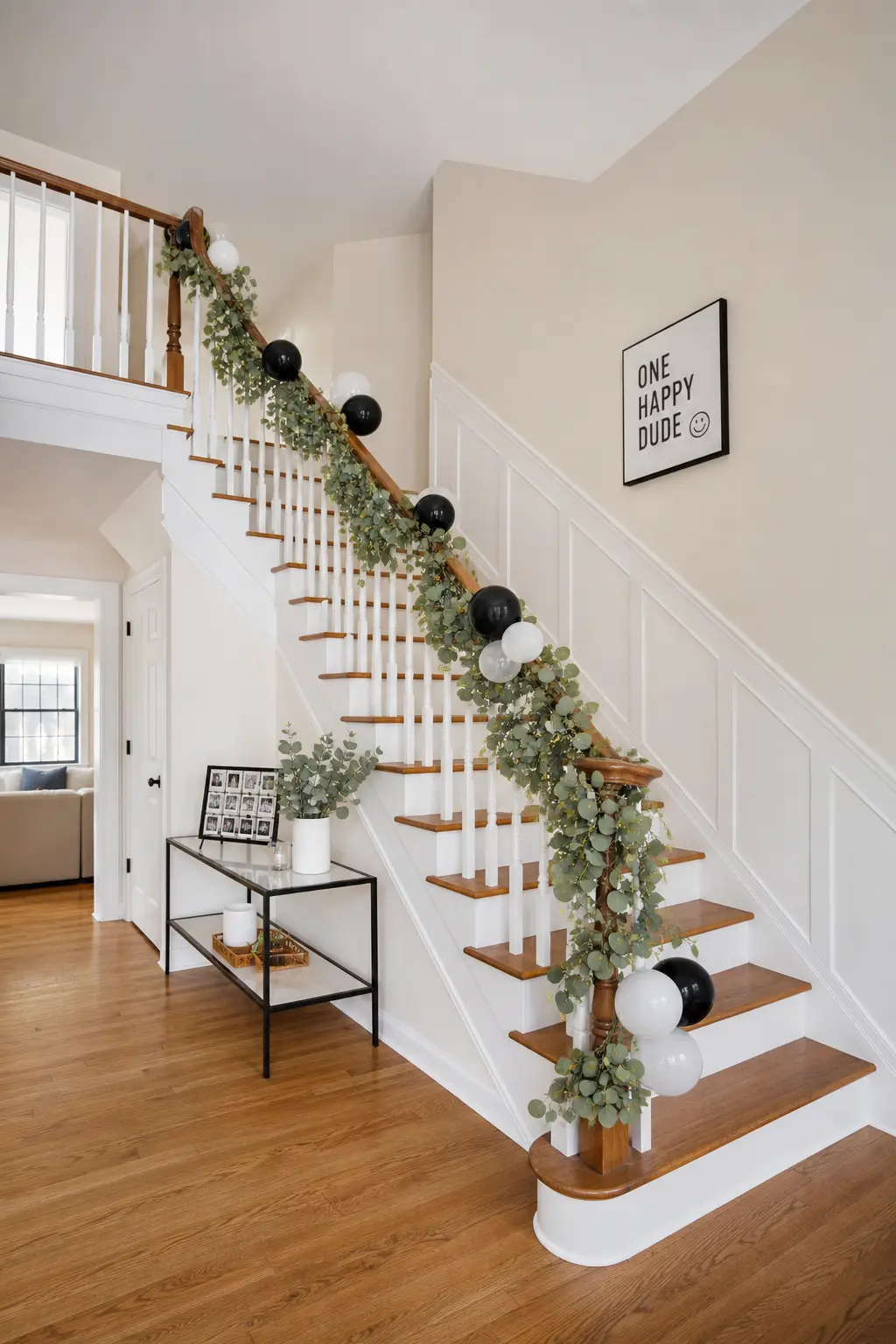 Greenery Garland With Balloon Insert — A eucalyptus garland draped along a staircase railing with black and white balloons tucked in at intervals gives you