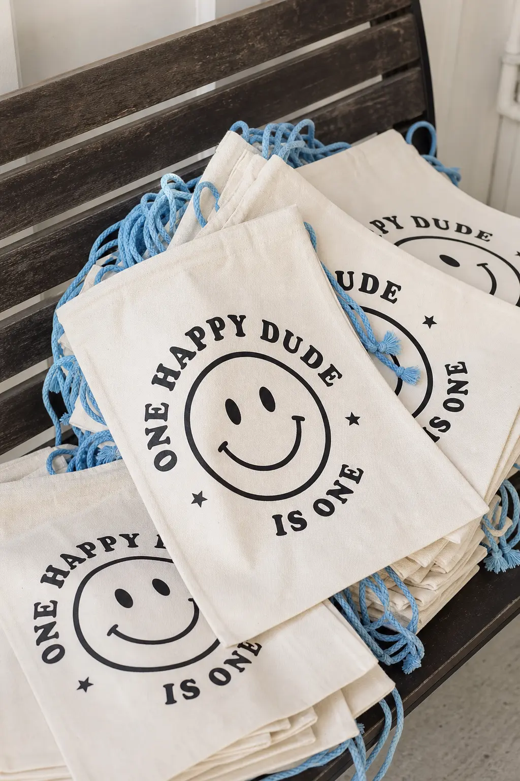 Retro Canvas Tote Favors — A stack of natural canvas totes printed with a black smiley and finished with sky blue drawstring cords gives guests a bag they will