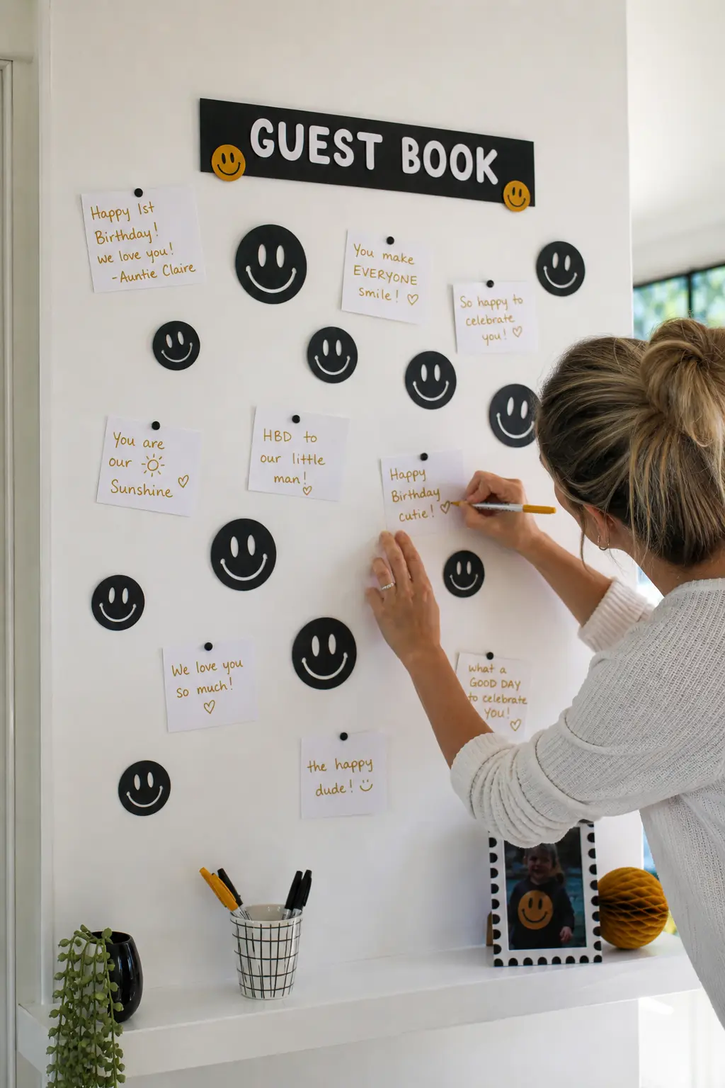 Smiley Guest Book Wall — A section of plain wall fitted with black smiley cutouts and a cup of mustard markers for guests to leave small pinned notes turns the