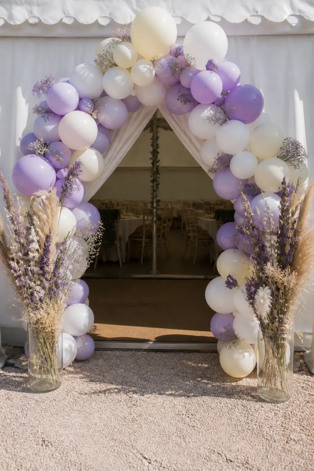 Lilac and Cream Arch at a Marquee Entrance with Dried Flowers at the Sides — A marquee entrance takes a larger arch than any indoor equivalent. Pastel balloon