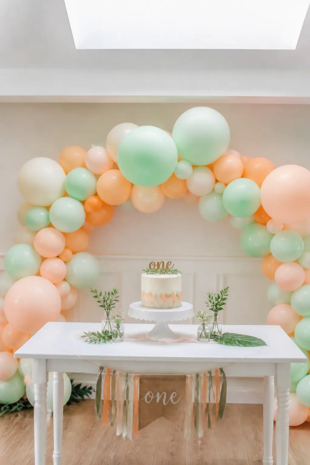 Mint and Peach Garland Behind a First Birthday Cake Table — Mint and peach is the colour pairing that feels fresh without trying. Pastel balloon arch