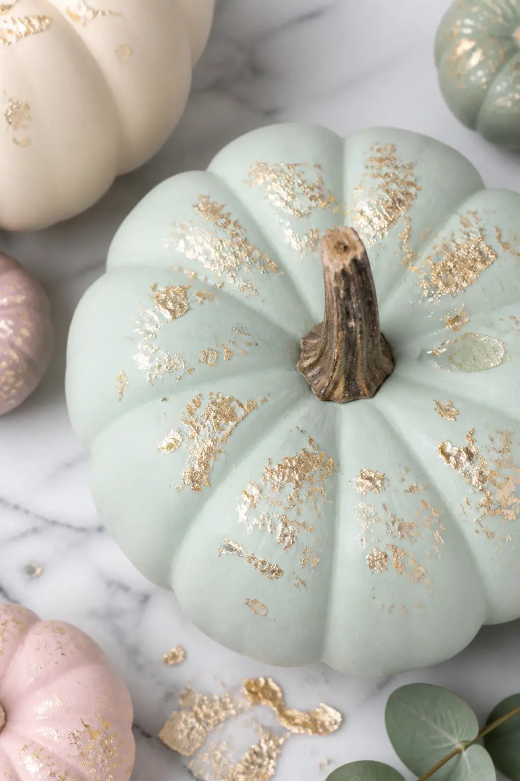 Gold Leaf Flecks on a Pale Base — Apply matte chalk paint in any pale pastel shade and allow it to dry. Pastel painted pumpkin