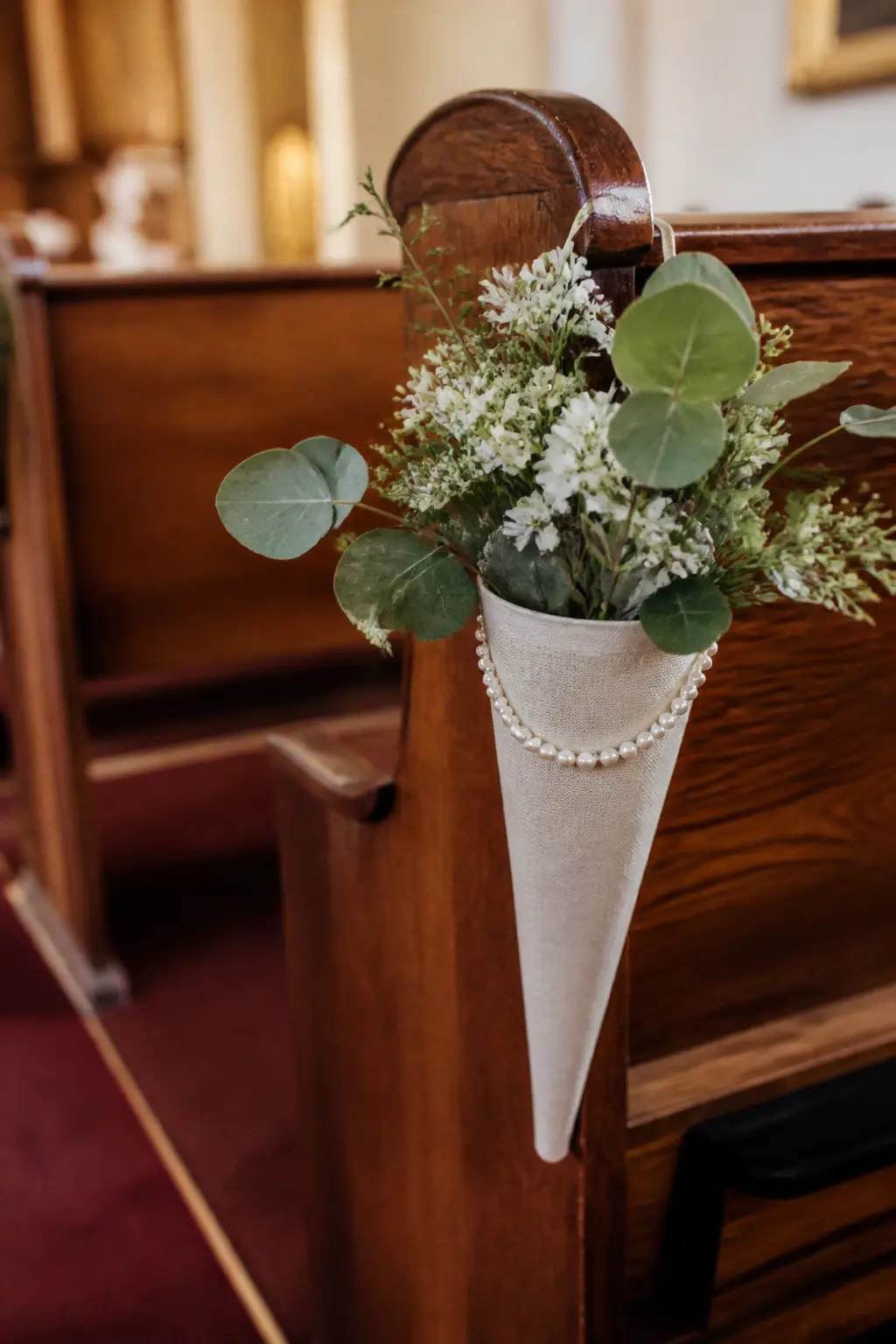 Pearl and Greenery Pew Cone — A small kraft-paper cone lined with a square of linen, filled with three stems of eucalyptus and baby's breath, and finished with