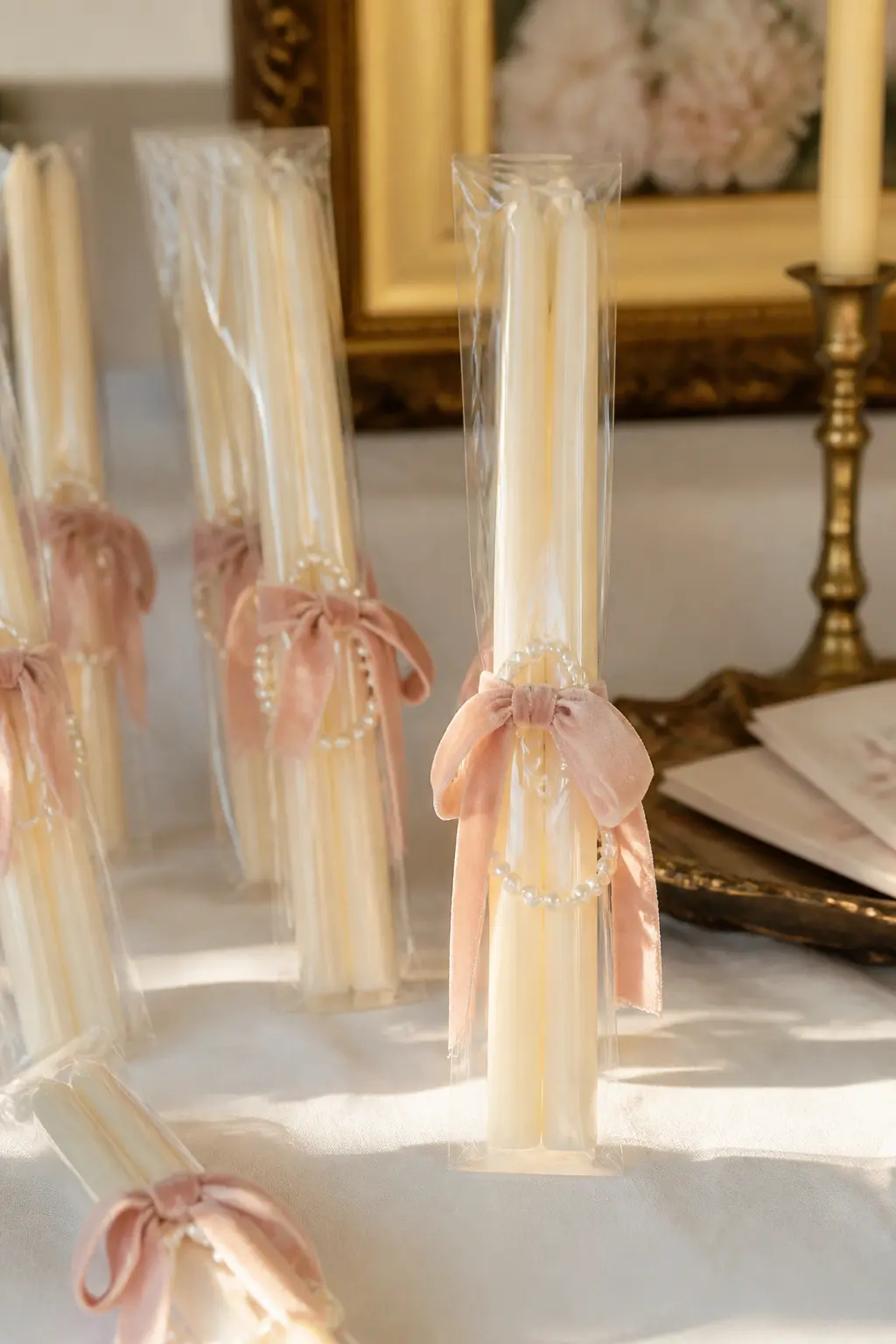 Pearl-Wrapped Taper Candle Favour — A pair of ivory taper candles bundled together with a strip of blush velvet ribbon, a small loop of pearl garland slipped