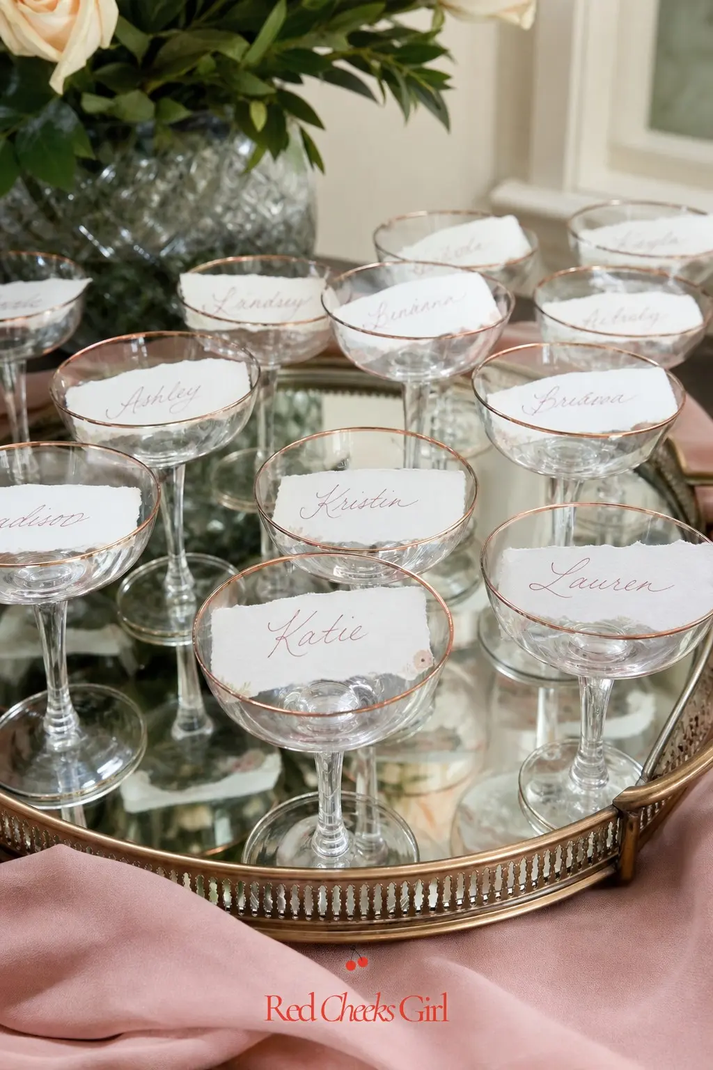 Escort Card Champagne Glass Display — A mirrored tray holding a row of small glasses, each one printed with a guest's name and standing in for a seating chart