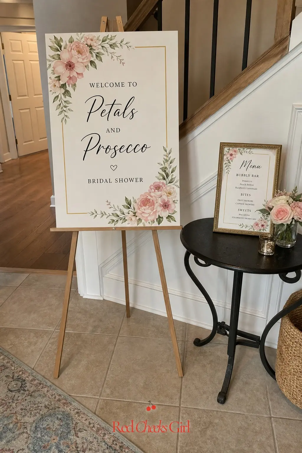 Floral Welcome Sign and Menu Signage — A wooden easel holding a cream sign, hand lettered in black script and framed with a thin gold border, tells guests the