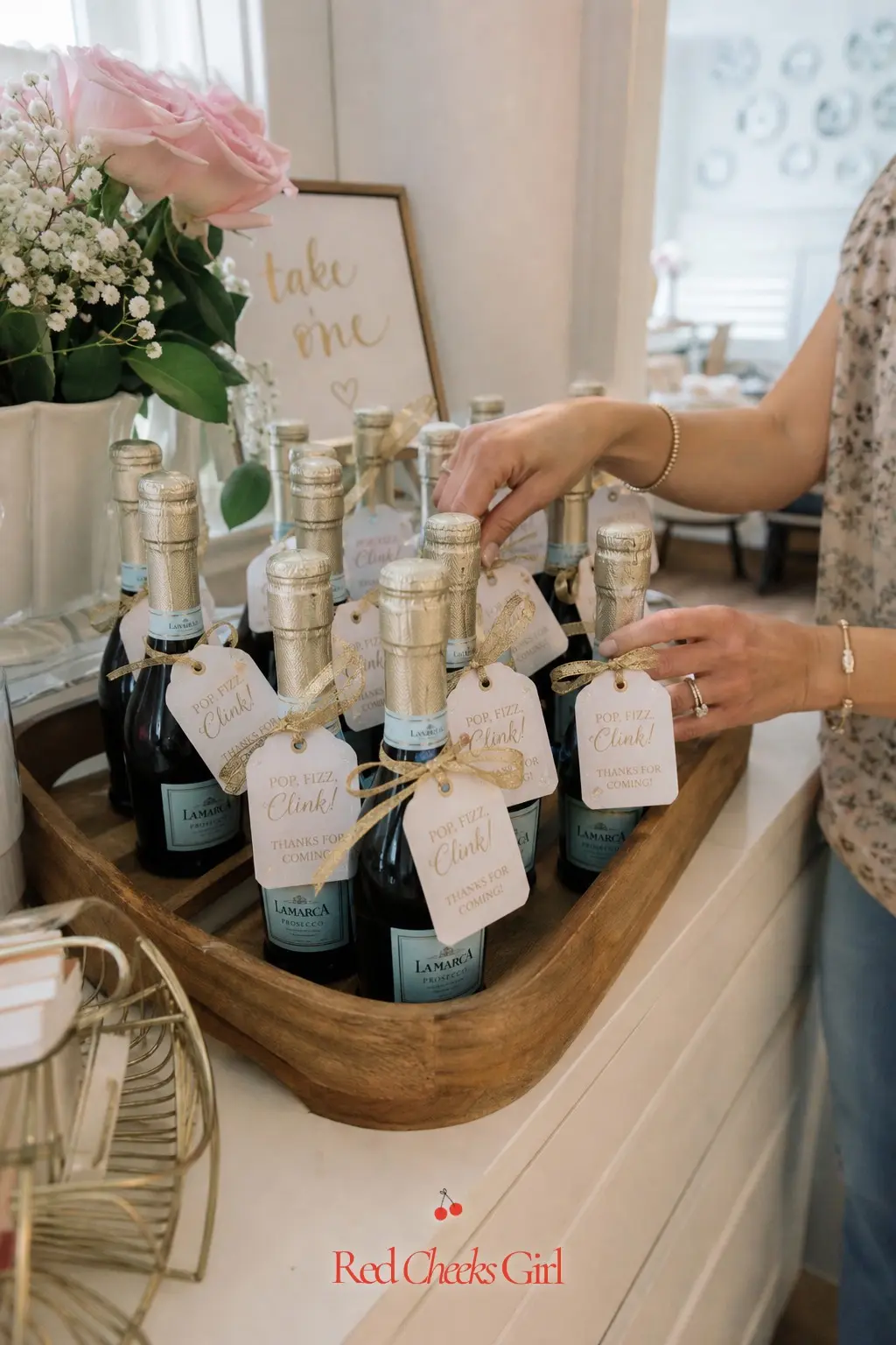 Mini Prosecco Favor Station — Small bottles lined up on a tray, each tied with a gold ribbon and a handwritten tag, let guests grab a favor on the way out