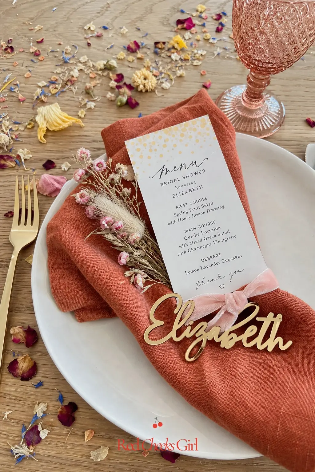 Petal-Scattered Place Setting — A single place setting, dressed with a terracotta napkin, a small name card and a scatter of petals around the plate, is the