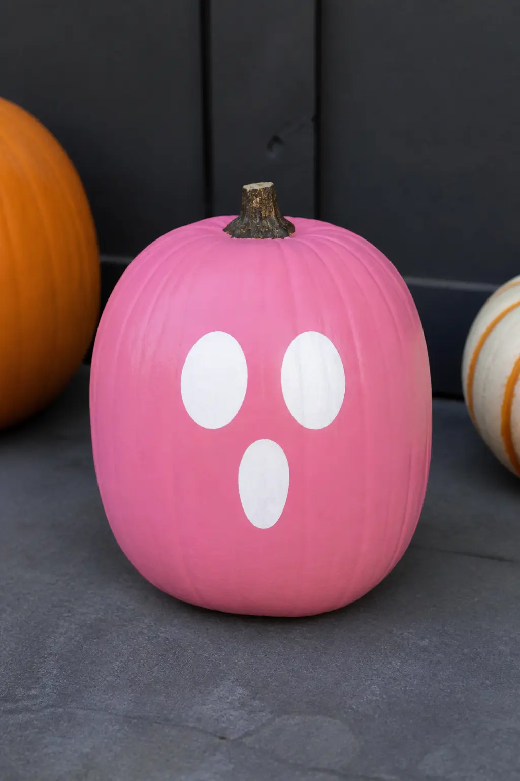 Mid Pink With a Ghost Face — Paint a simple ghost face in white on the front of the pumpkin: two round eyes and a small oval mouth, all in solid white with no