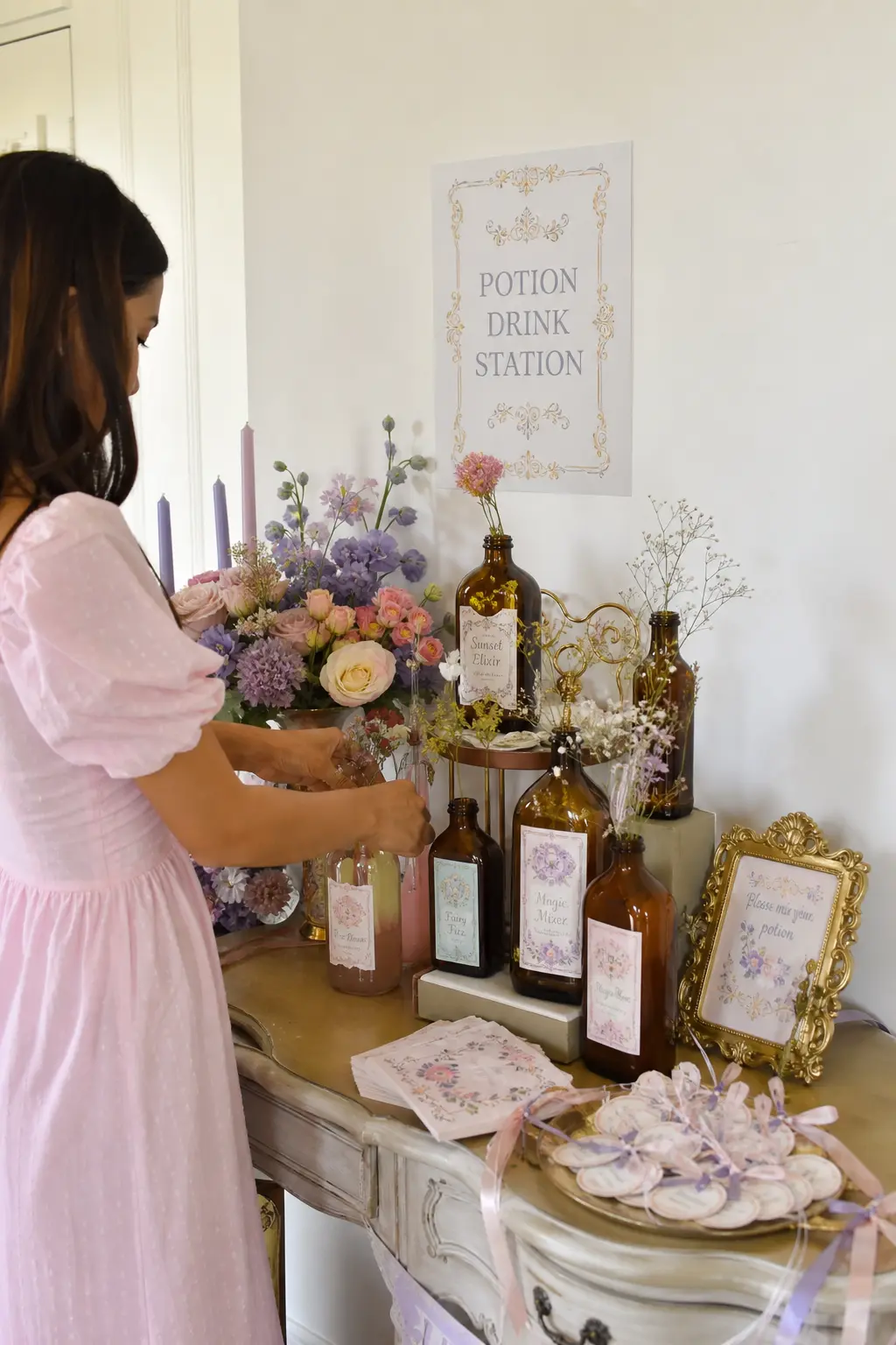 Bottled Potion Drink Station — Amber glass bottles filled with sage and blush tinted drinks, dressed with dried flower sprigs and hand-lettered paper labels