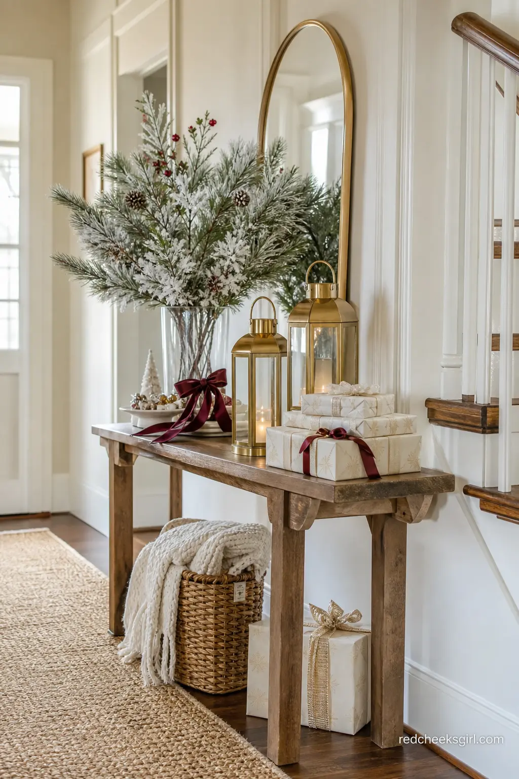 Flocked Pine Welcome Console with Brass Lanterns — A narrow console just inside the door holds flocked pine branches in a tall glass vase, flanked by two lit
