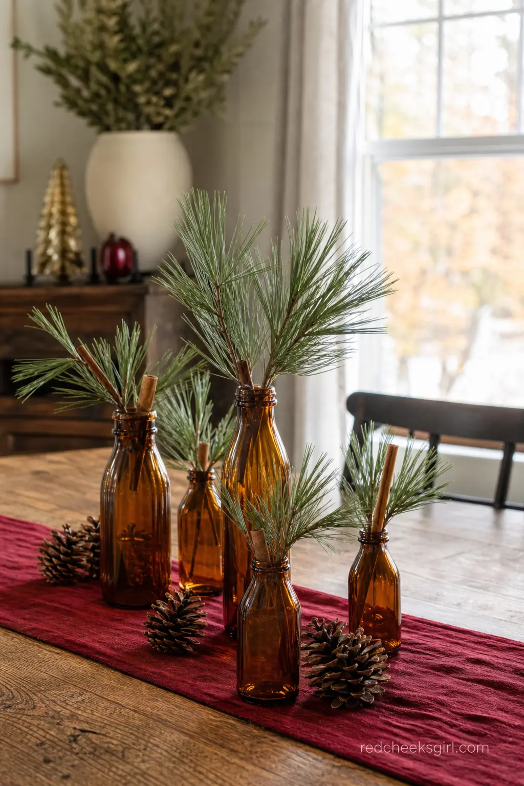Milk Bottle and Pine Sprig Centerpiece — A cluster of amber glass milk bottles holds sprigs of pine and a few cinnamon sticks at the center of a long wood