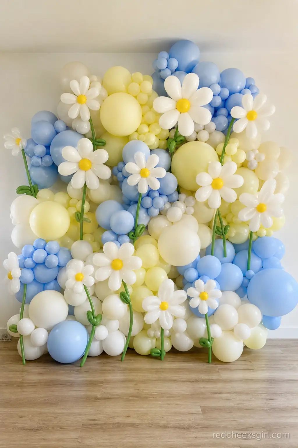 Daisy Balloon Wall — A dense wall of white daisy stems interspersed with pale yellow and periwinkle balloon clusters fills one full wall, floor to a