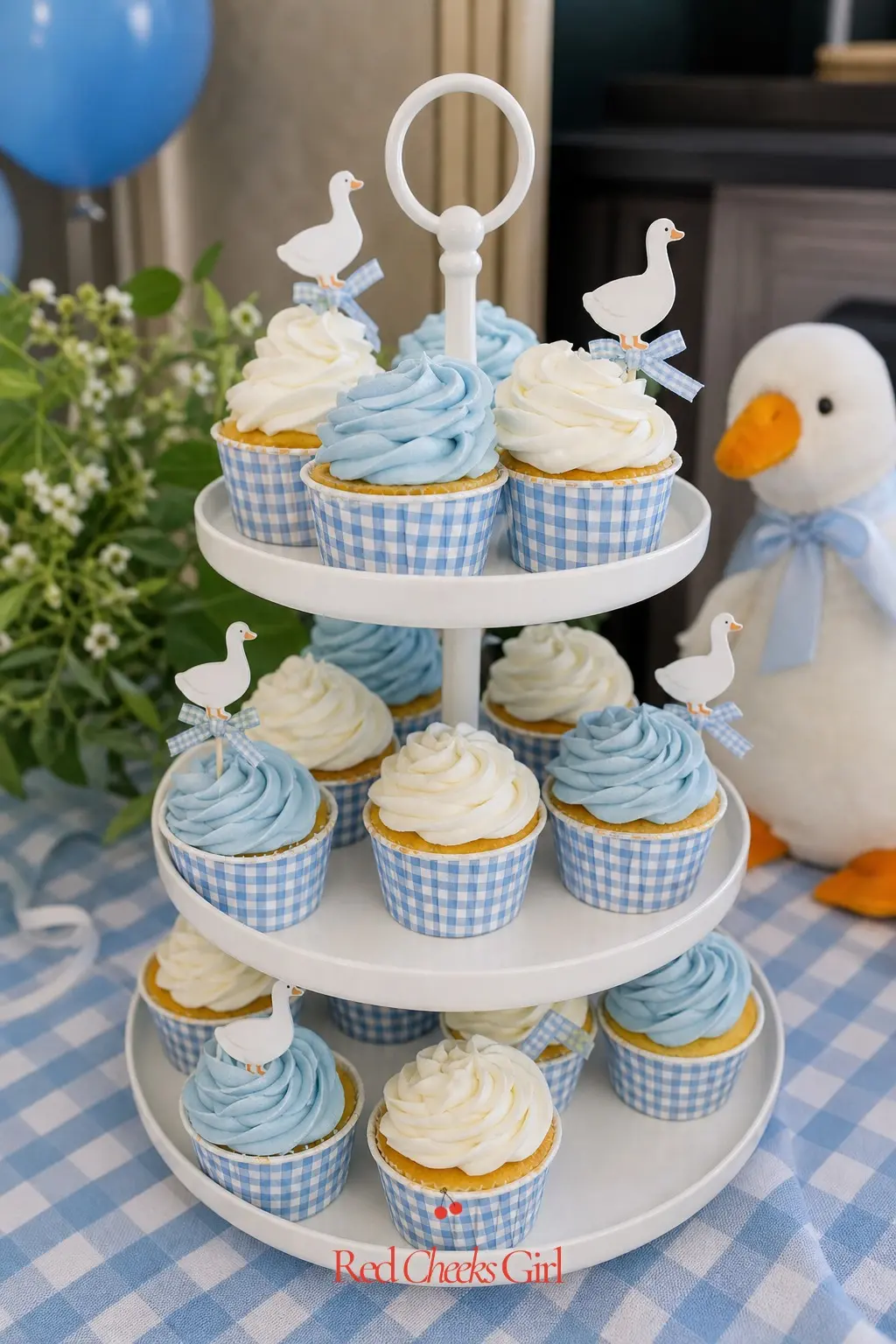 Gingham Cupcake Tower — A tiered white stand holds cupcakes frosted alternately in white and pale periwinkle, with goose picks in only a few and small gingham