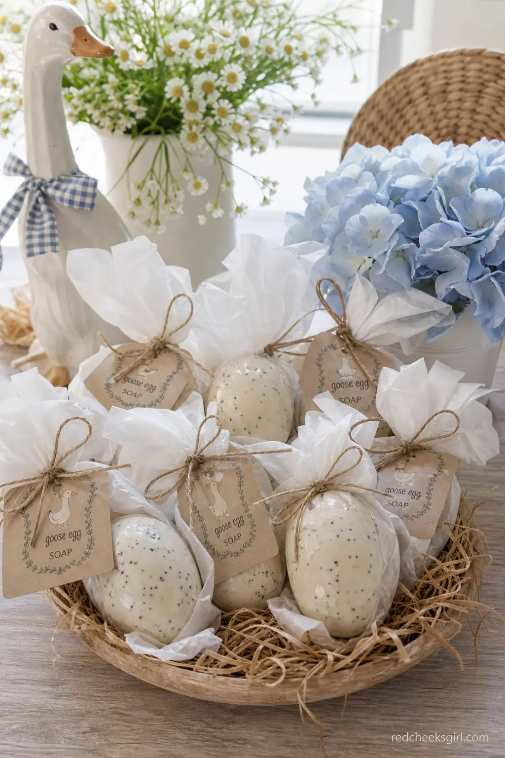 Goose Egg Soap Favors — Small oval bars of soap, molded and tinted to look like pale speckled goose eggs, sit in a shallow wooden nest, each one wrapped in