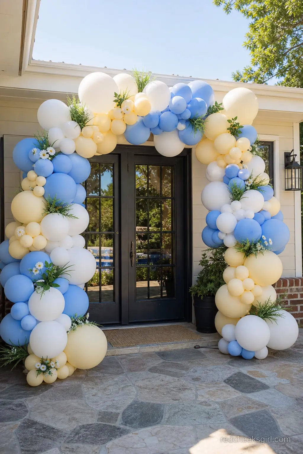 Goose Garden Balloon Arch — An organic balloon arch in buttercream yellow, periwinkle blue and white curves over the entrance, with a few faux grass tufts