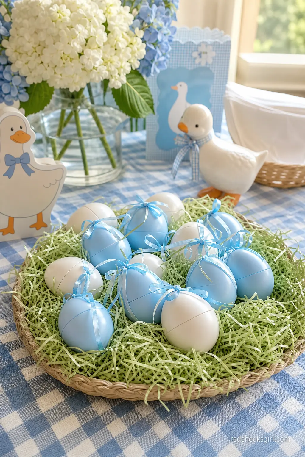 Nesting Favor Box Table — Small egg-shaped favor boxes in white and periwinkle sit nestled in shredded paper grass inside a low basket, each one tied shut with