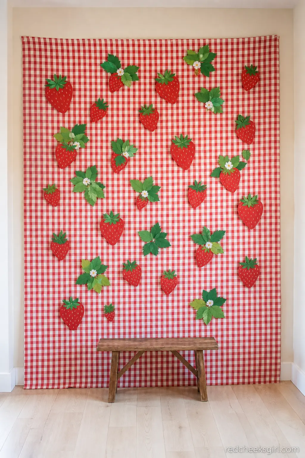 Gingham Wall Backdrop With Paper Strawberries — Red and white gingham fabric pinned flat across a wall gives you an instant backdrop without a rented frame.