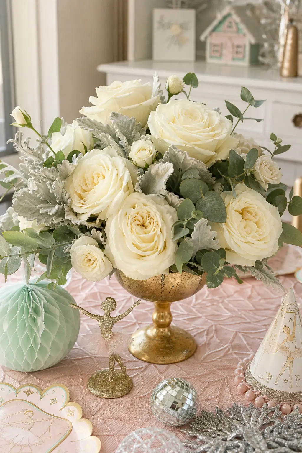 Ivory Rose Centerpiece Bouquets — A gold compote vase overflows with ivory garden roses, silvery dusty miller and pale eucalyptus, set at the center of a guest