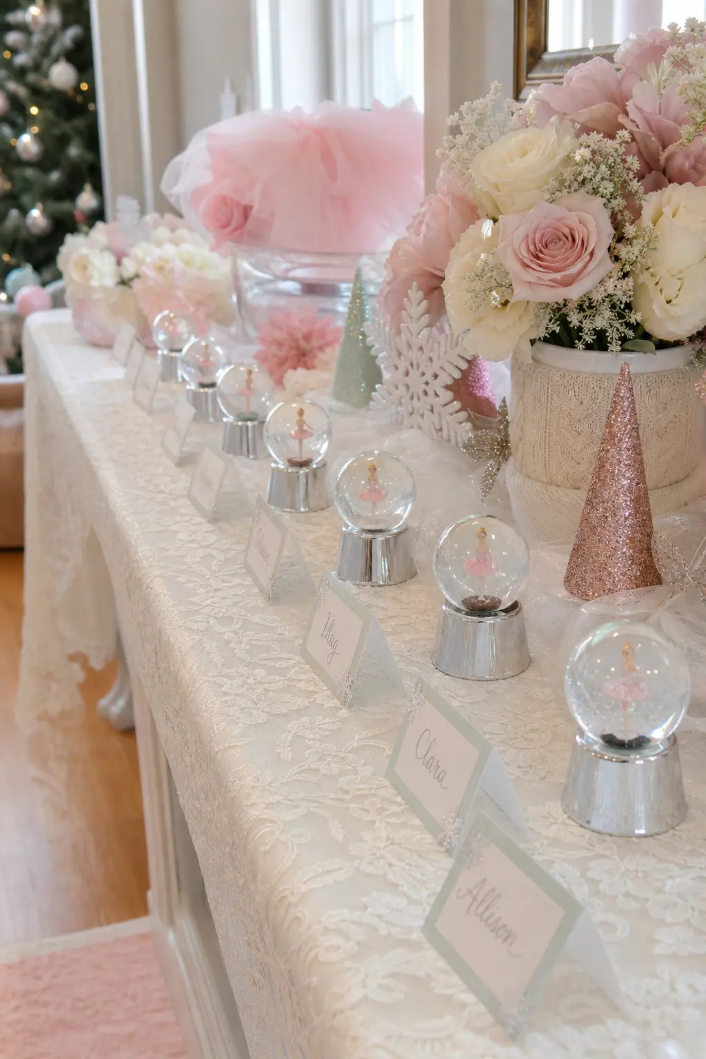 Mini Snow Globe Favor Table — A narrow table dressed in an ivory lace runner holds a tidy row of small snow globes, each sitting beside a handwritten name tag.