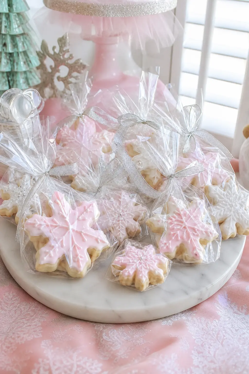 Sugarplum Cookie Favor Bags — Snowflake shaped sugar cookies, glazed in pink and white, sit in clear cellophane bags tied off with silver ribbon and laid out