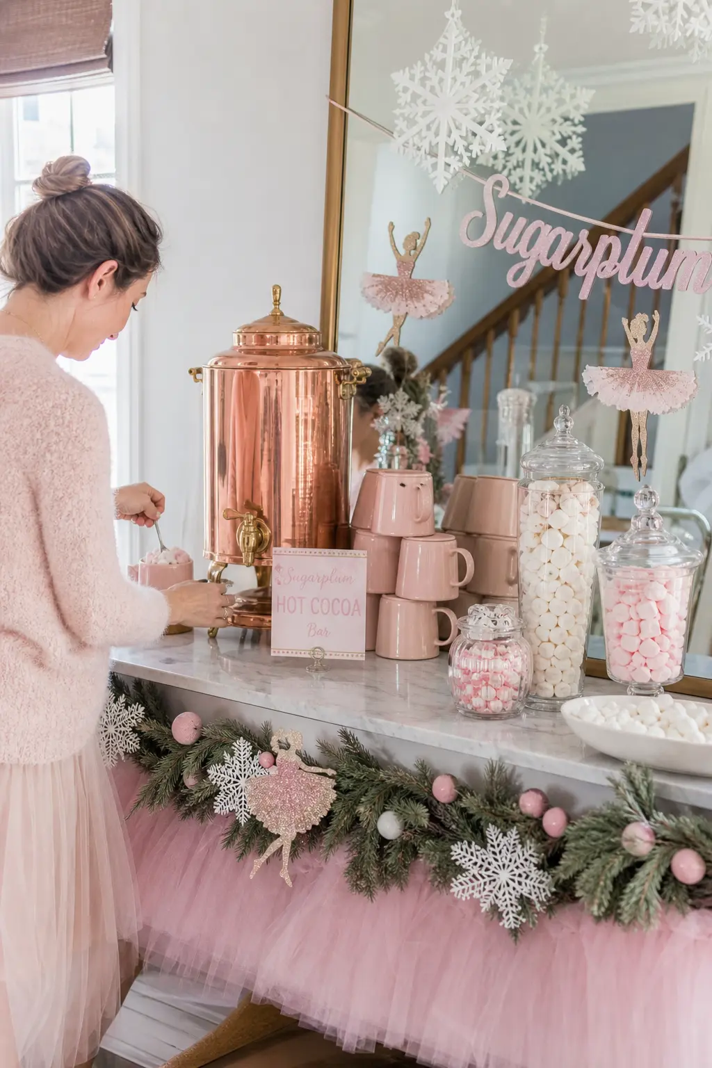 Sugarplum Hot Cocoa Bar — A hot cocoa station on a marble console holds a copper dispenser, a stack of blush mugs and small jars of pink and white