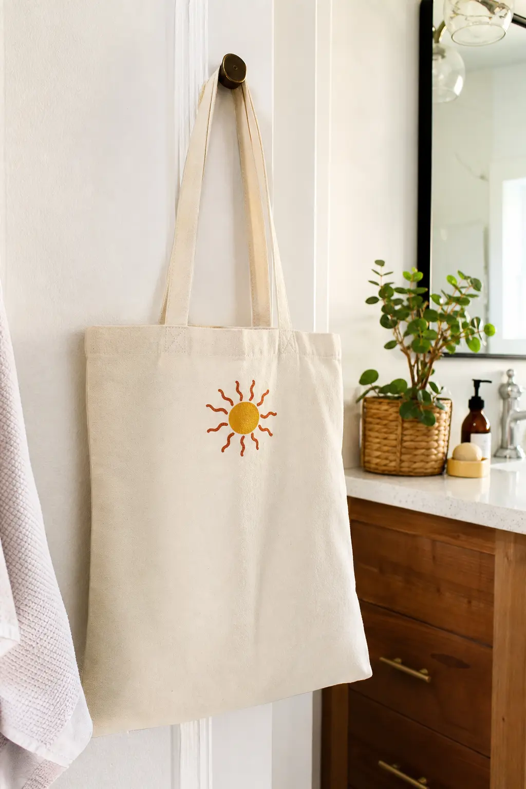 Wavy Sun Icon Tote — A simple round sun with short wavy rays, painted in mustard with thin rust orange outlines, sits high on one shoulder of a cream canvas