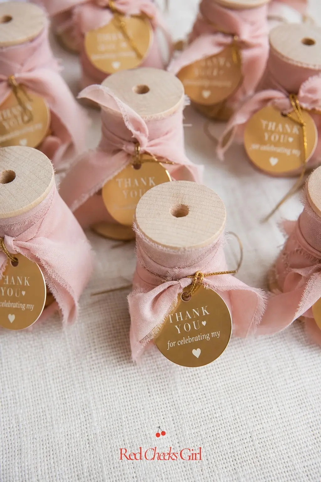 Ribbon Spool Favor Tags — A small spool of ribbon, tagged with a round gold favor label, gives every guest something genuinely useful rather than another