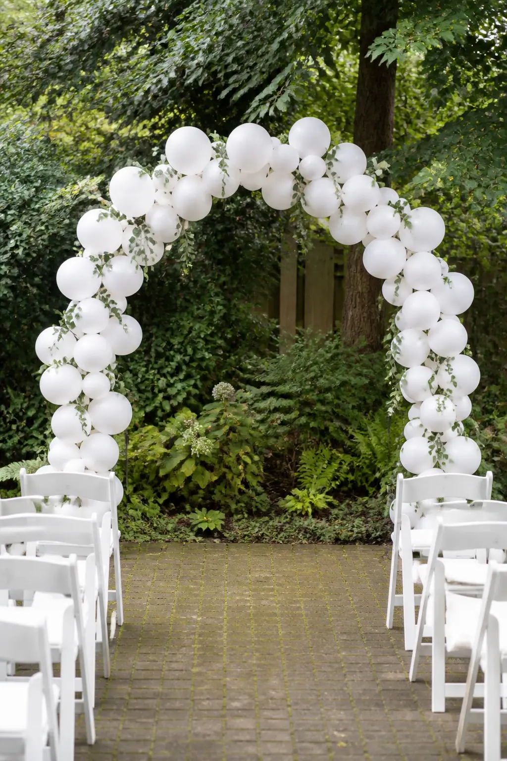 White and Eucalyptus Over a Garden Ceremony Spot — A white arch stands over a garden ceremony spot, eucalyptus threaded through it from base to base with no