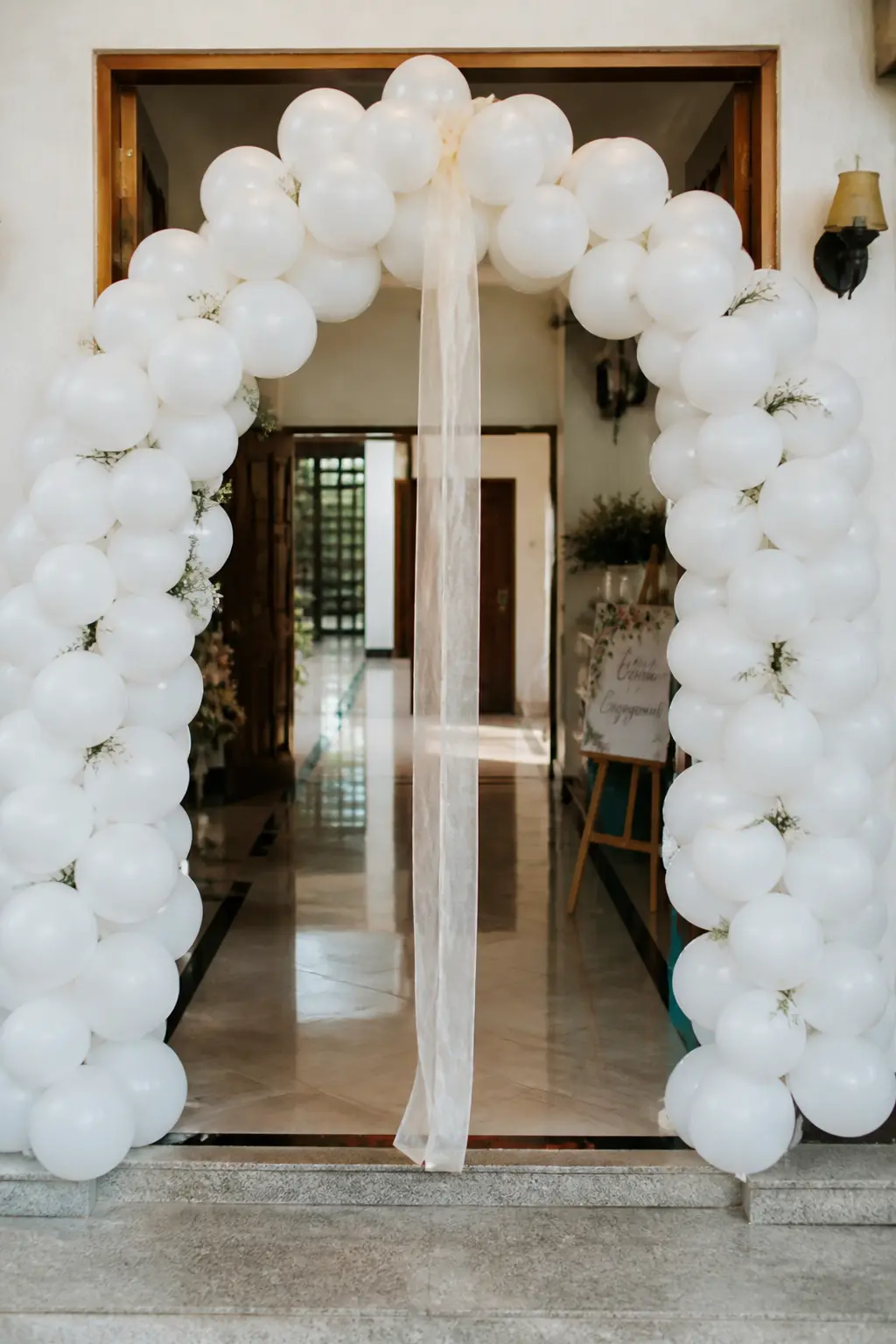 White Arch with a Single Ribbon Streamer from the Top over an Engagement Party Entrance — A single wide ribbon falling from the apex of an entrance arch is the