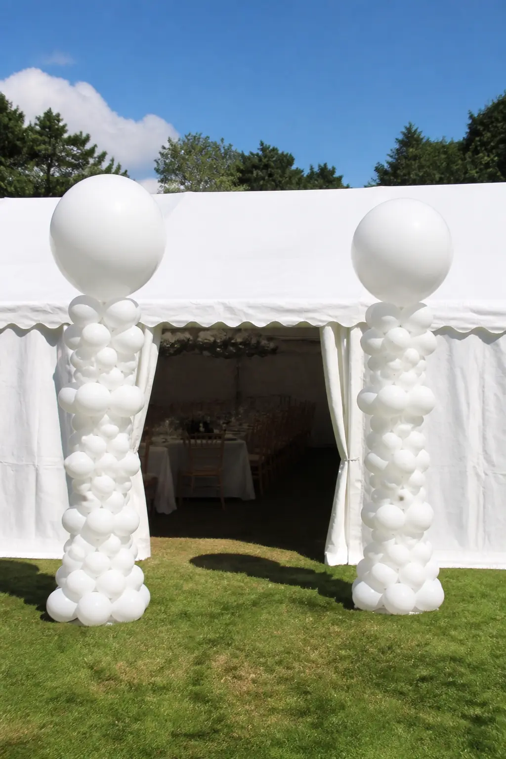 White Columns Either Side of a Marquee Entrance — Two balloon columns flanking a marquee entrance give the outside of the tent the same moment of arrival as an