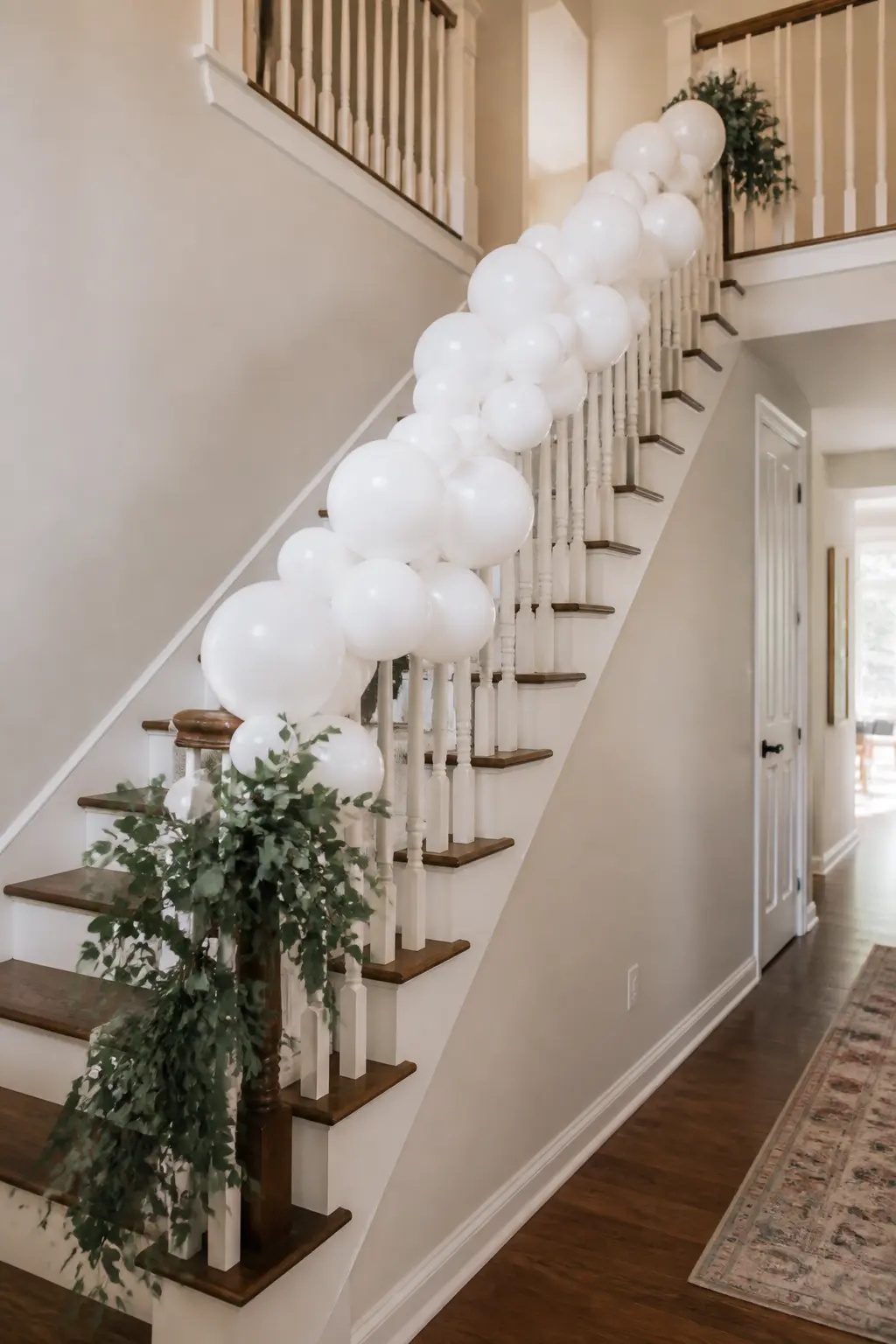 White Garland with Greenery Only at the Base Along a Stair Banister — A stair banister garland has to travel a distance and stay in place through a full event.
