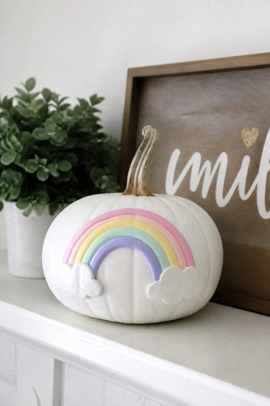 Pastel Rainbow Arc — A simple rainbow arc painted in pastel pink, yellow, mint and lilac sits in the lower half of the pumpkin face, with small white clouds at
