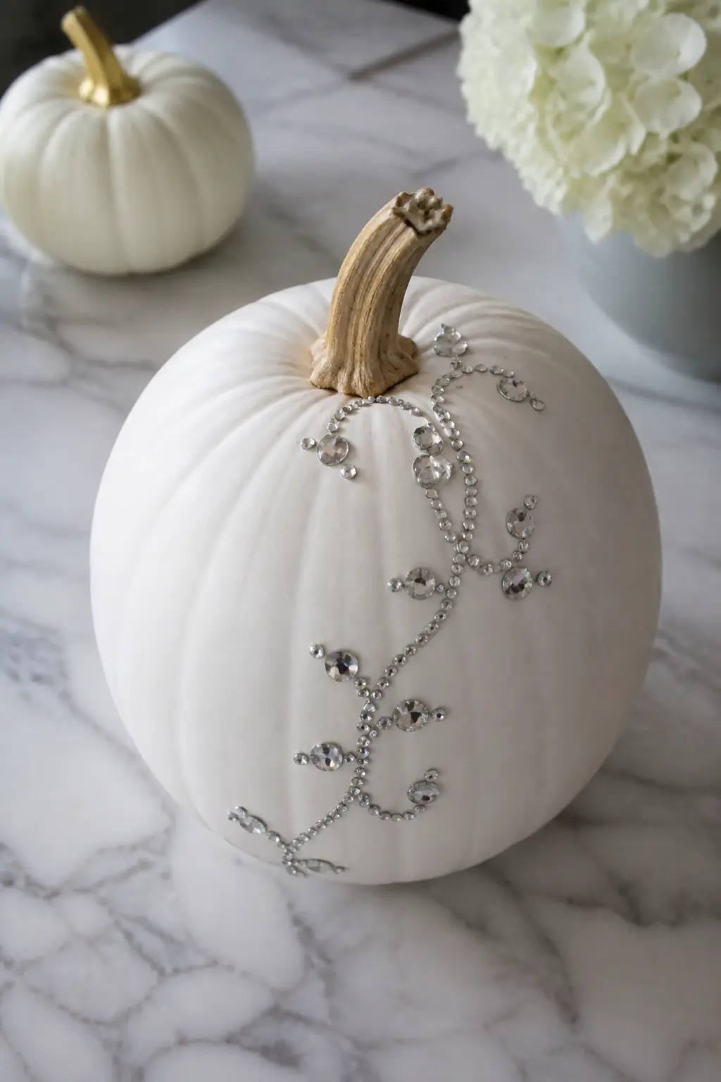 Rhinestone Curving Vine — A vine of flat-back clear rhinestones curves from the stem down to the base of the pumpkin in a loose S-shape. White painted pumpkin