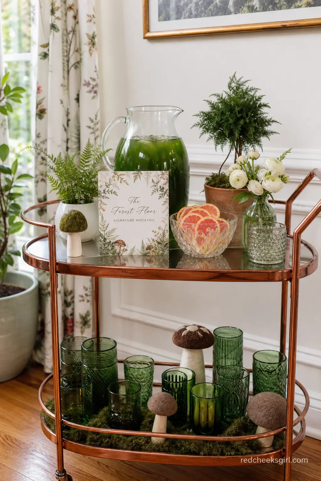 A Signature Mocktail Cart Called The Forest Floor — A copper bar cart holding a pitcher of a deep green herbal mocktail, a bowl of blush citrus wheels and a