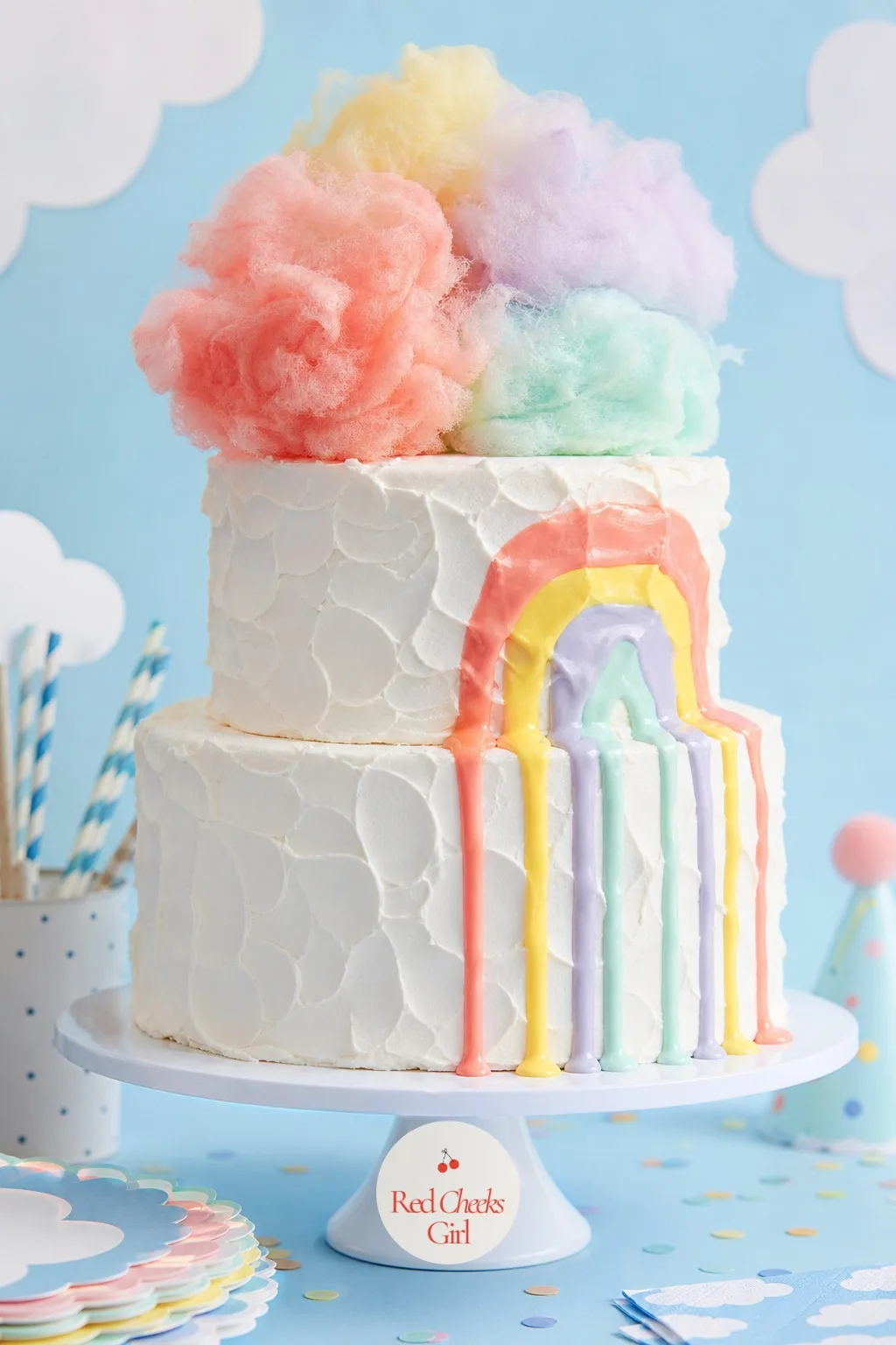 The Floating Rainbow Cloud Cake — Two round tiers underneath, frosted white and textured into soft peaks so the whole cake reads as sky rather than as cake.